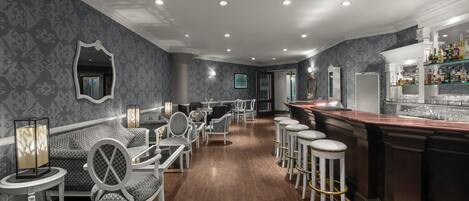Zona de bar con piso de madera, taburetes blancos y mostrador.