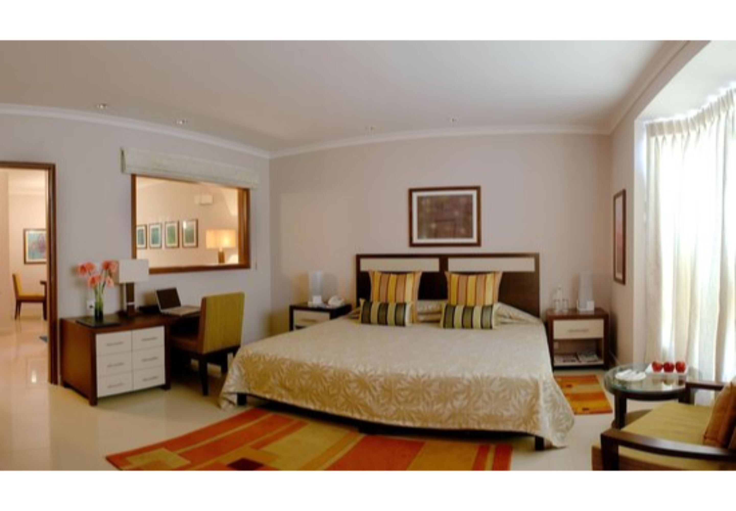 A hotel room with a large bed, a desk, a chair, a nightstand, and a window with curtains.