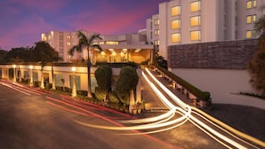 Um hotel moderno com uma placa de destaque, entrada bem iluminada e um acesso arborizado.
