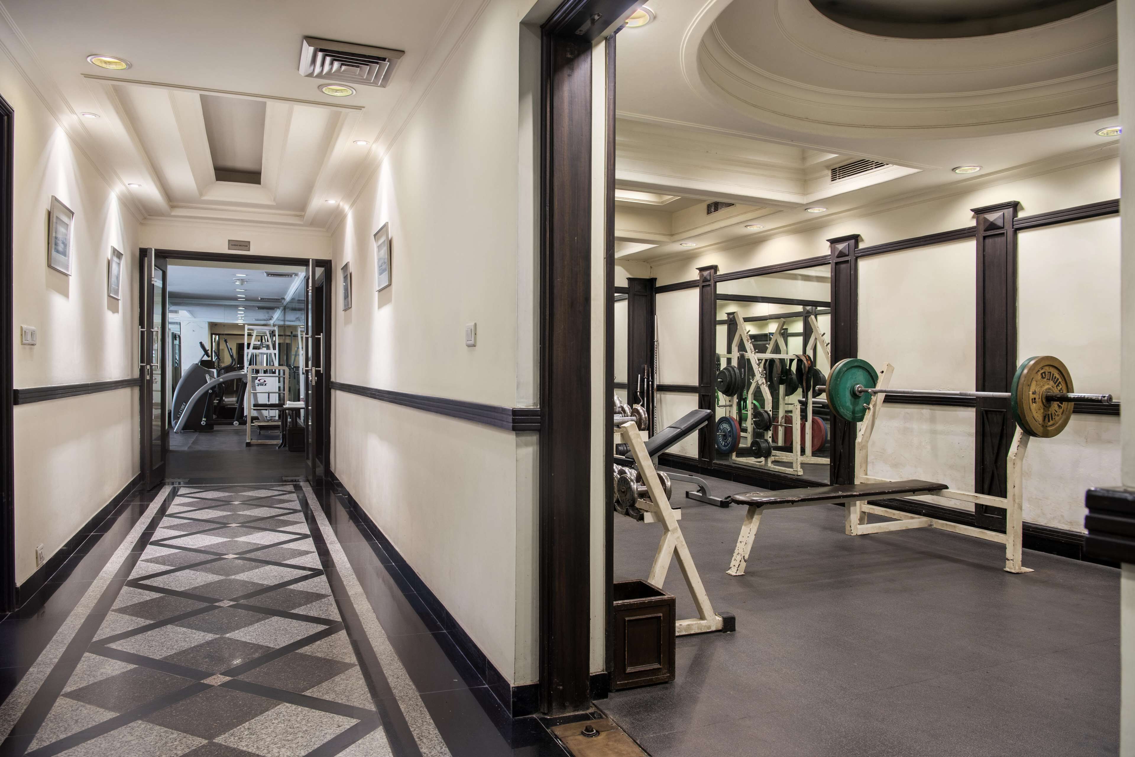 Une salle de sport équipée de matériel de musculation et un couloir dont le sol est recouvert d’un revêtement à motifs.