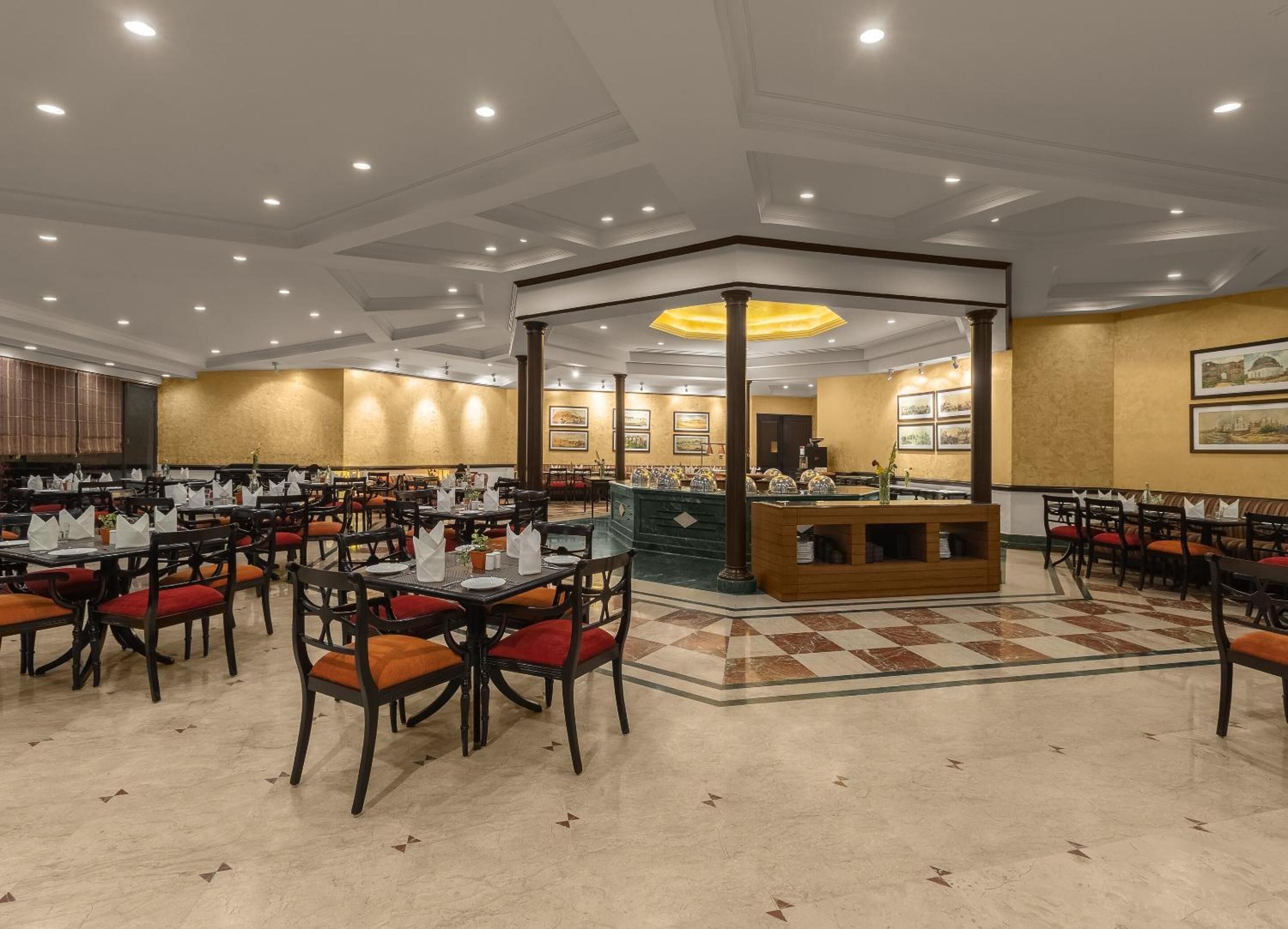 Een ruime eethoek met meerdere tafels en stoelen, een centraal buffet en een plafond met inbouwverlichting.