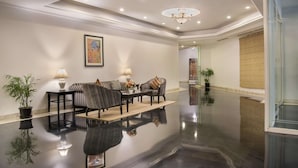 Um lobby moderno com piso lustroso, um conjunto de sofás, um candelabro e uma obra de arte emoldurada na parede.