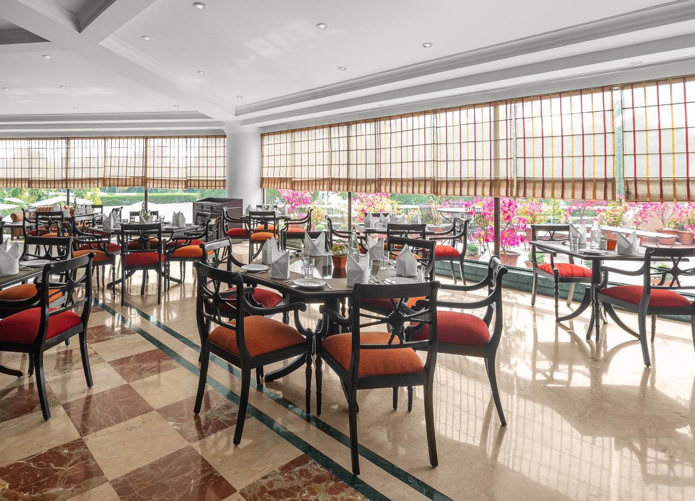A spacious dining area with multiple tables and chairs, large windows with decorative grills, and a tiled floor.