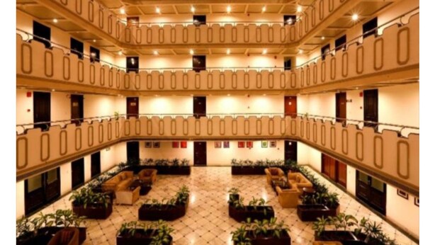 Um saguão de hotel em vários níveis, com um espaço aberto central, várias áreas de estar e piso ladrilhado.