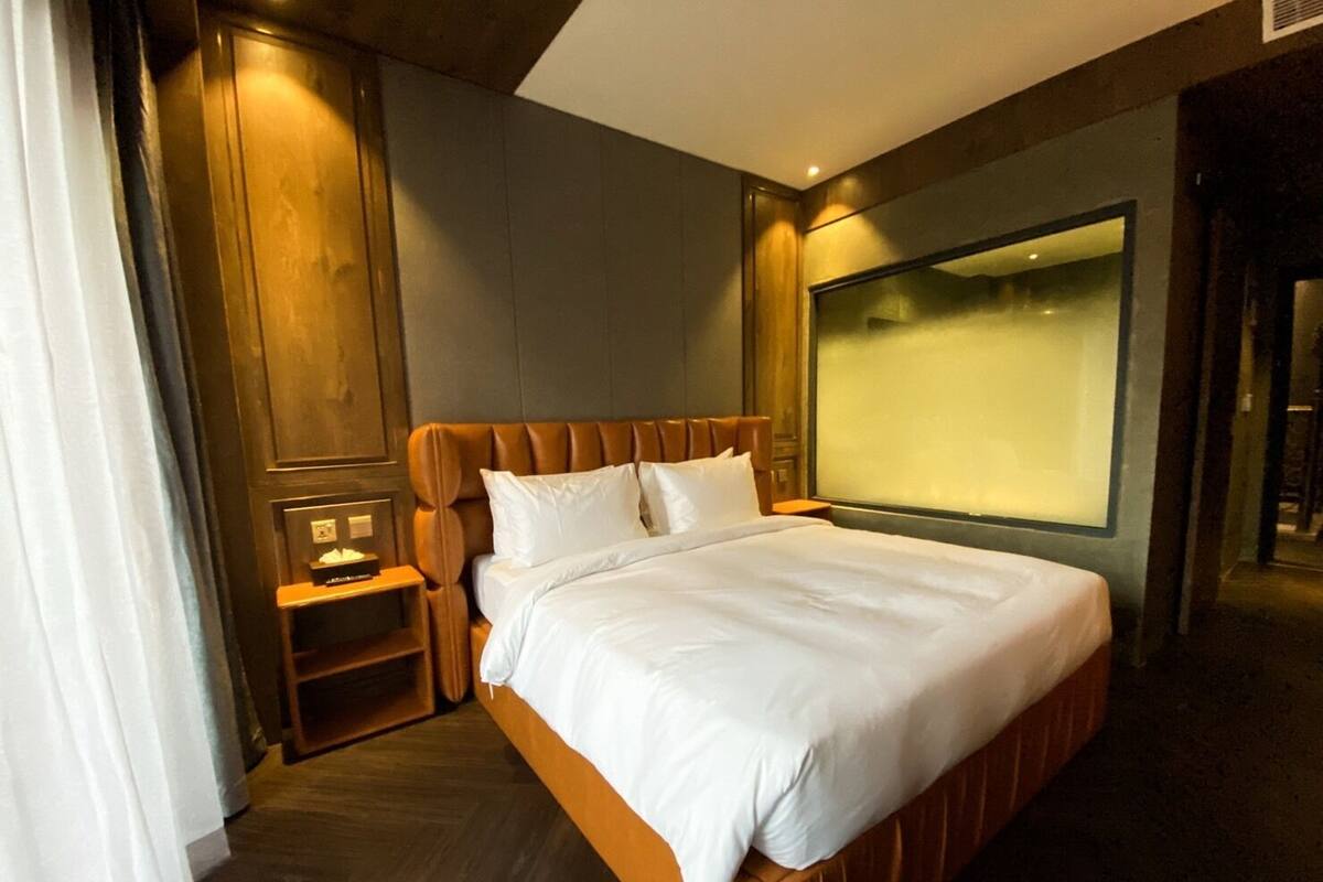 A modern hotel room with a large bed, wooden headboard, and a large window.