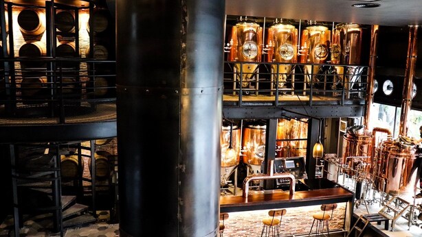 A multi-level bar with exposed industrial elements, including copper tanks and wooden barrels. - CHECK inn Phnom Penh BKK 1 (Phnom Penh)