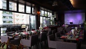 A restaurant with a long table set for dining, large windows, and a stage with musical equipment. - CHECK inn Phnom Penh BKK 1 (Phnom Penh)