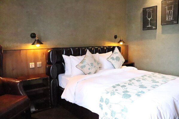 Quarto de hotel com uma cama, uma mesinha de cabeceira, uma luminária e uma parede com quadros.
