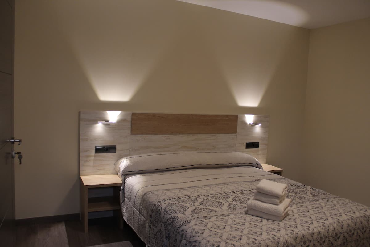 A hotel room with a bed, bedside tables, and a headboard with integrated lighting.