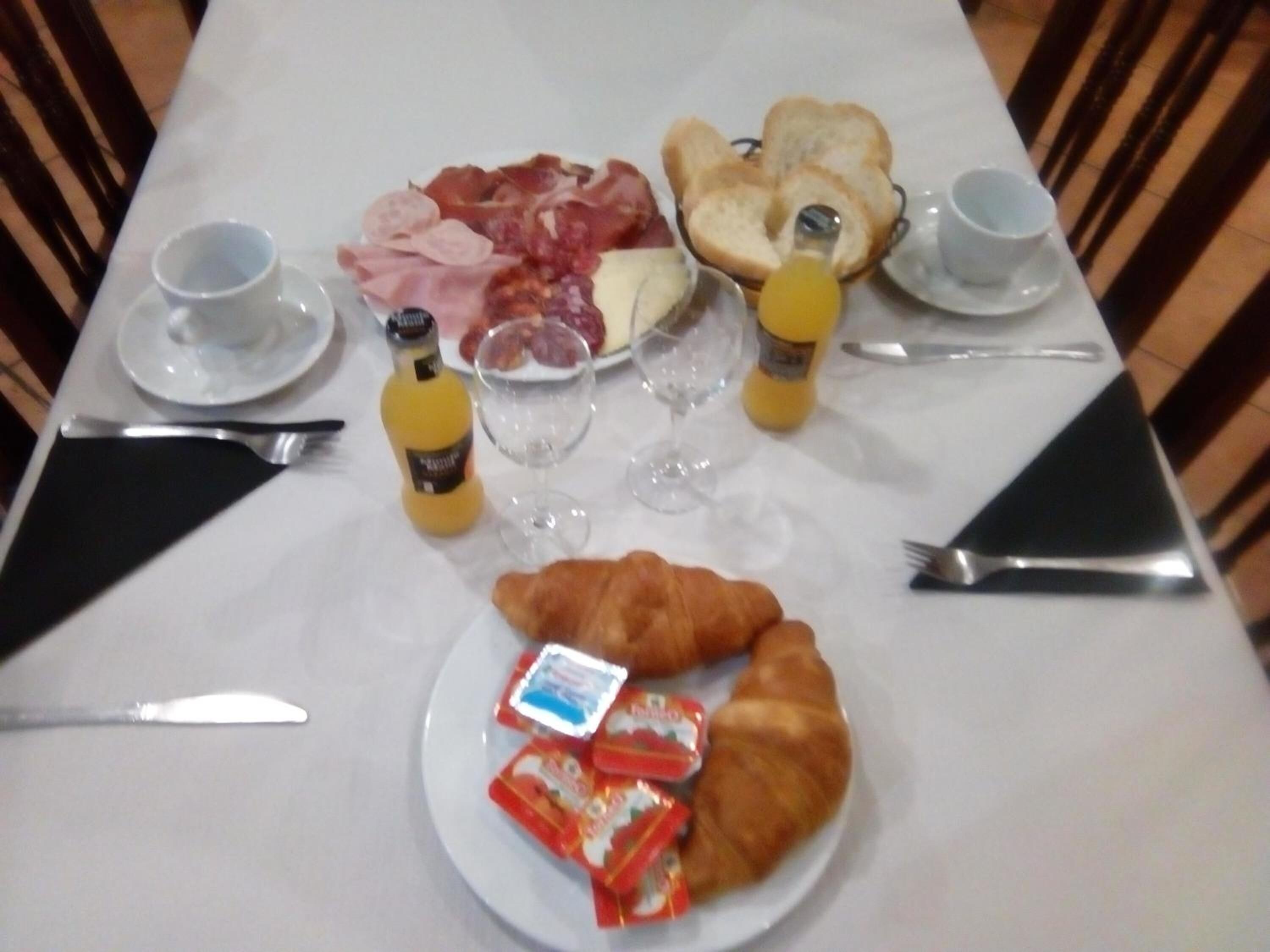 A breakfast table with croissants, ham, cheese, bread, and juice.