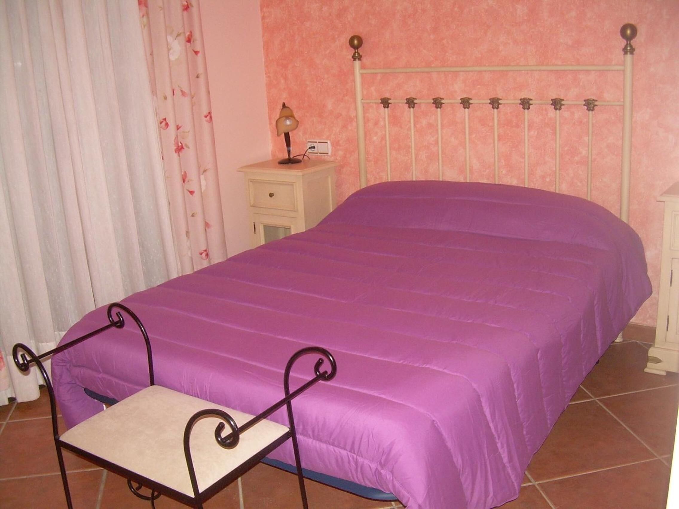 A bedroom with a bed, a nightstand, a lamp, and a chair.