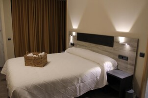 Habitación de hotel con una cama grande, cabecera con iluminación integrada, mesita de noche y una cesta de mimbre sobre la cama.