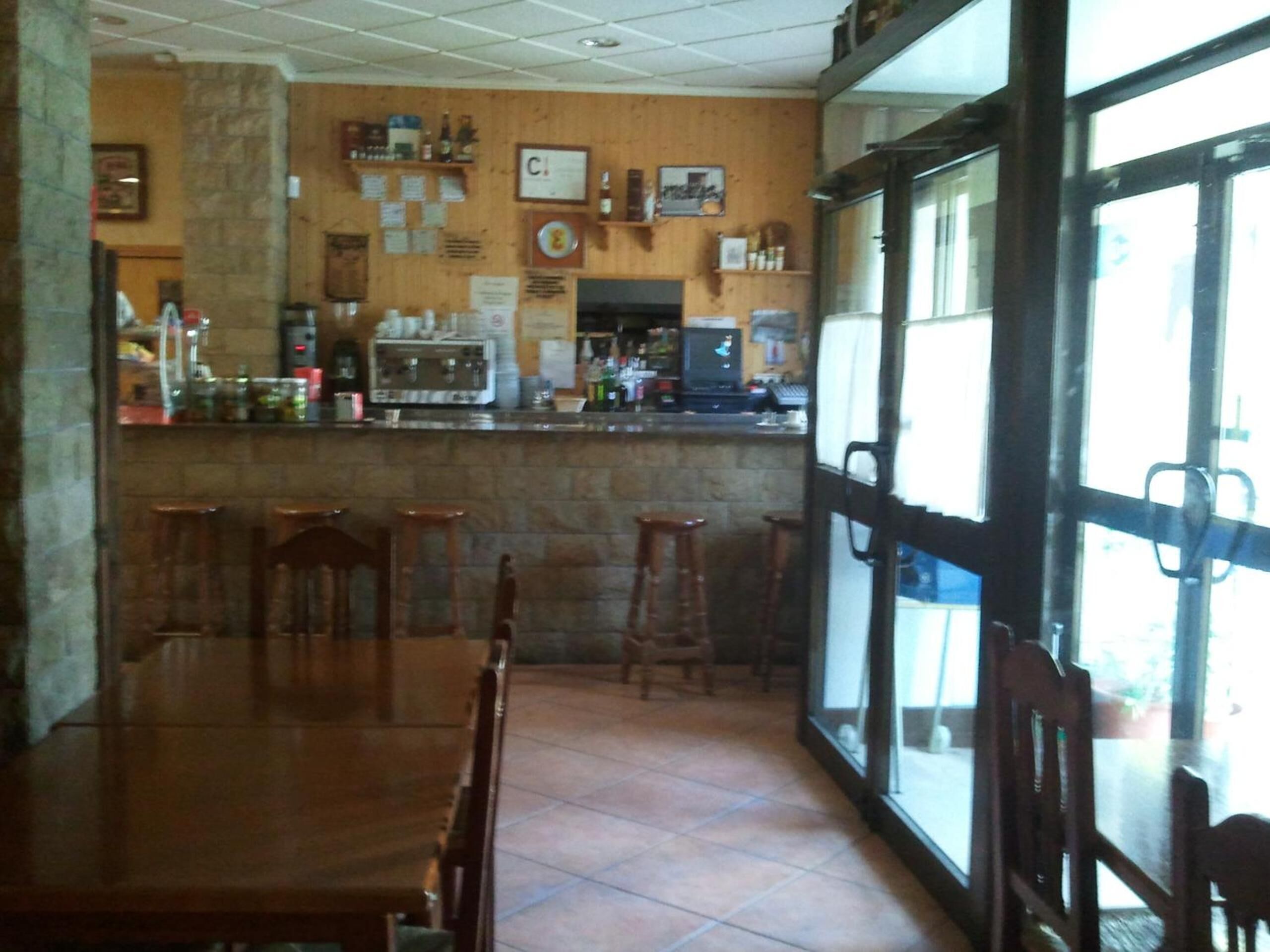A restaurant with a bar area, wooden tables and chairs, and a tiled floor.