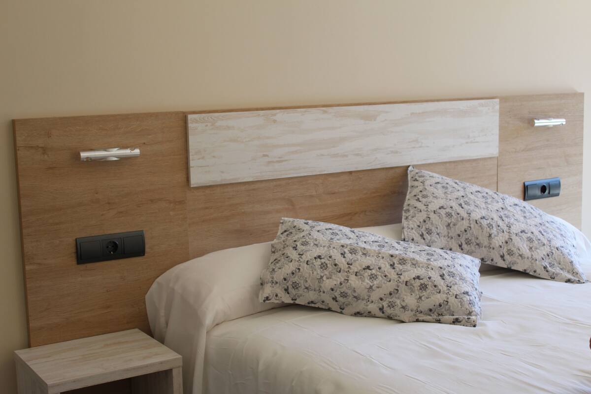A bed with a wooden headboard, two floral-patterned pillows, and a bedside table with a drawer.