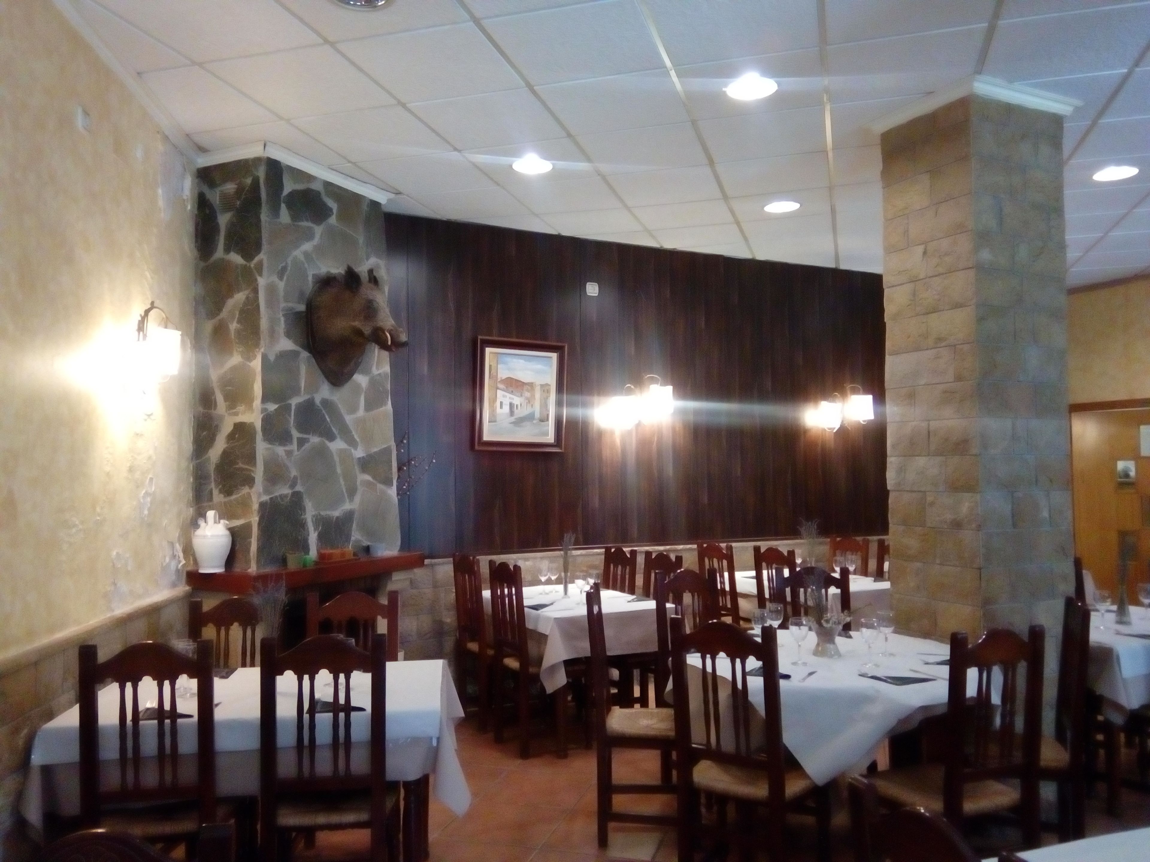 A restaurant with stone walls, wooden chairs, and tables set for dining.