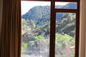 Una ventana con vistas a un paisaje montañoso, cortinas medio corridas y marco de madera.