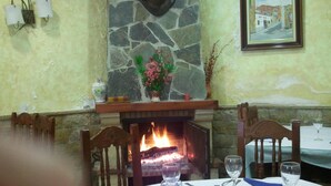 A dining area with a stone fireplace, a framed painting, and a table set for two with wine glasses and cutlery. - Ca L'angels (Prat de Comte)