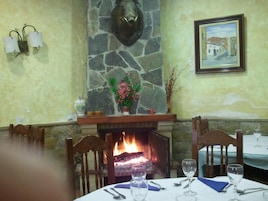 Un comedor con chimenea de piedra, un cuadro enmarcado y una mesa para dos personas dispuesta con copas de vino y cubiertos.