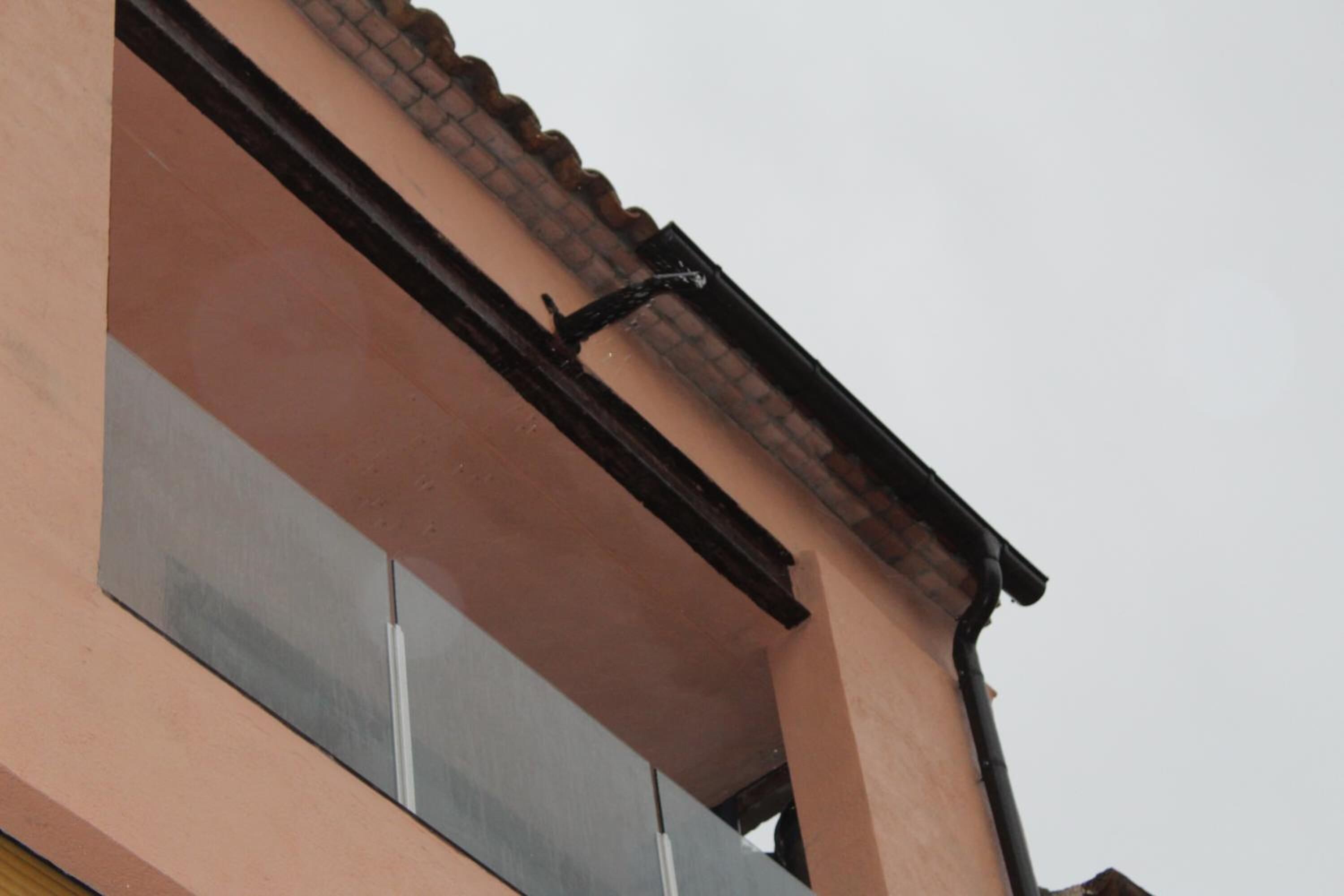 Un edificio con fachada rosa, techo de tejas y bajante negro.