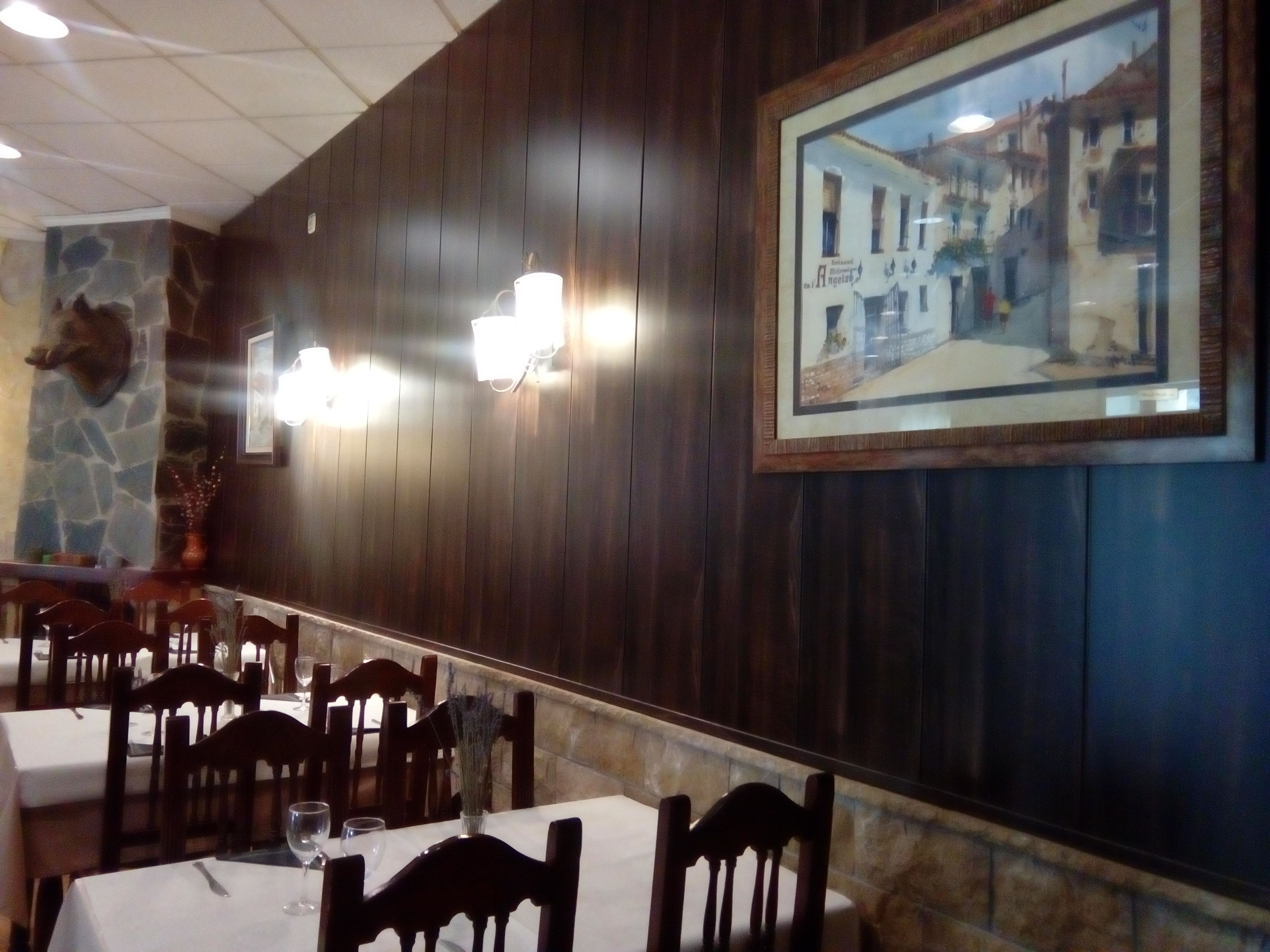 A restaurant with wooden panel walls, stone accents, and framed artwork. Tables are set with white tablecloths and chairs.