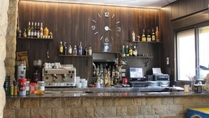 A bar area with a clock on the wall, shelves with bottles, a coffee machine, and a computer monitor. - Ca L'angels (Prat de Comte)