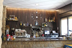 Zona de bar con un reloj en la pared, estantes con botellas, una máquina de café y un monitor de computadora.