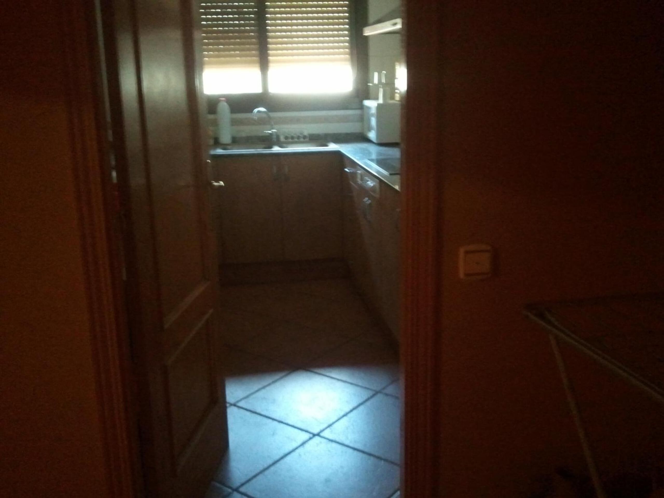 Una cocina estrecha con suelo de baldosas, una ventana con persianas y un lavabo.