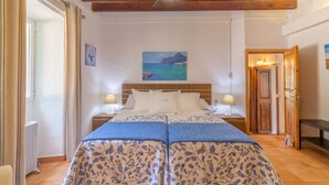 A double bed with floral bedding, a ceiling fan, and a painting of a coastal scene. - Aire Can Pieres, Finca 5StarsHome Mallorca (Esporlas)