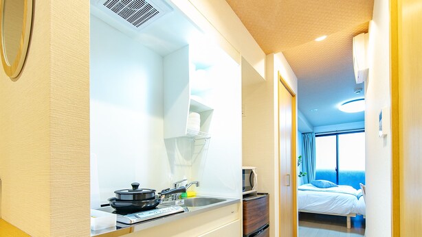 A modern kitchen with a microwave, stove, and cabinets. There is a bed with a window in the background. - F Plus Inn Tofukuji (Kyoto)
