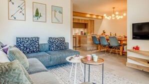 Una sala de estar moderna con un sofá gris, una mesa de centro y un comedor con sillas y un televisor.