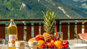 Una mesa con una botella de vino, frutas y tazas de chocolate, con montañas al fondo.