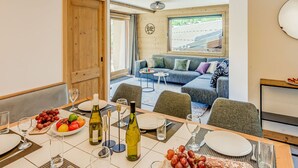 Un comedor con una mesa dispuesta para dos, un sofá al fondo y vistas al exterior.