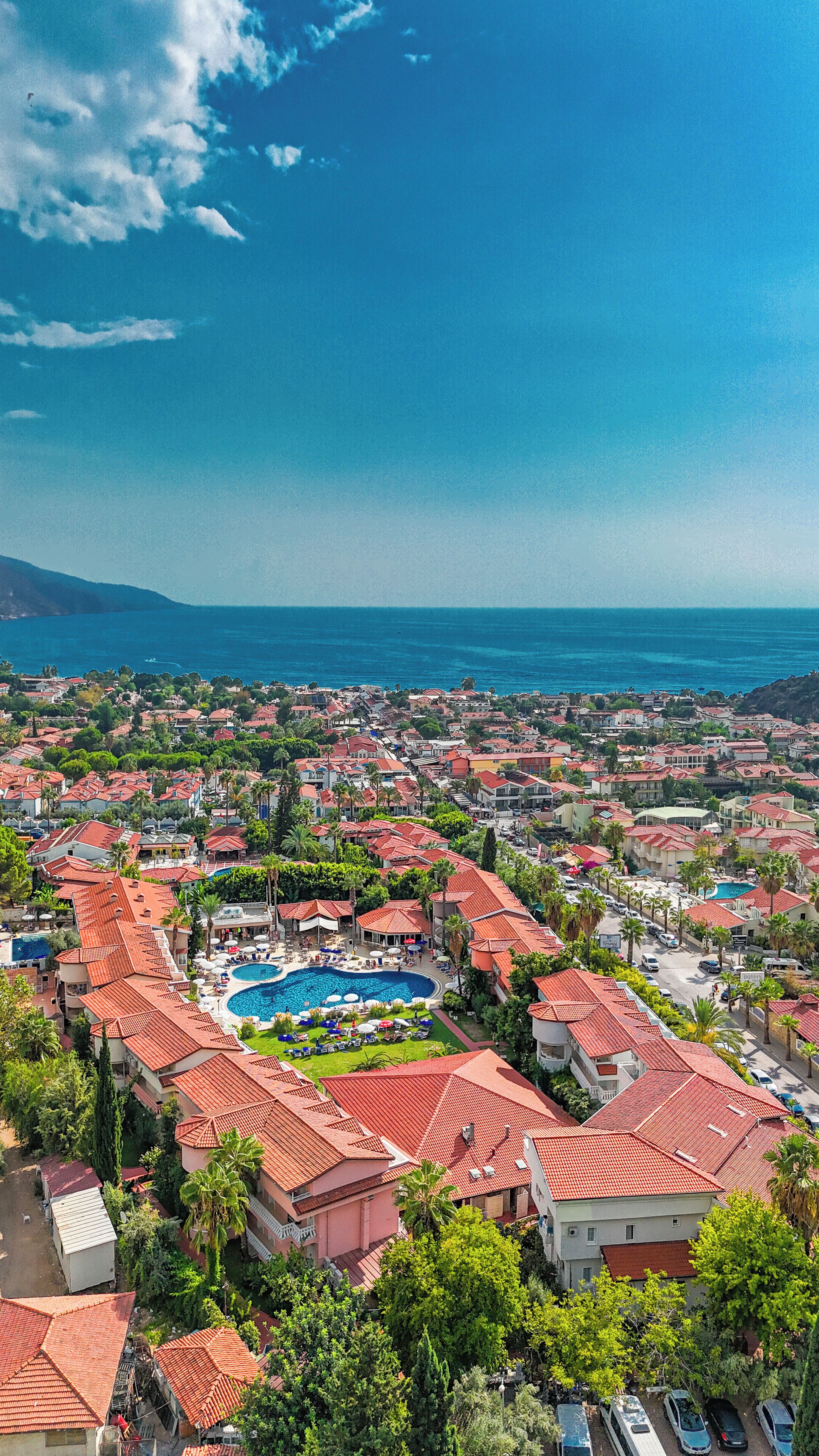 Ein Küstenresort mit roten Dächern, einem zentral gelegenen Pool und Blick auf das Meer.