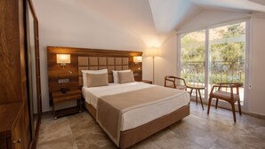 A bedroom with a large bed, bedside lamps, a nightstand, a chair, and a view of the outdoors through a glass door. - Ölüdeniz Turquoise Hotel (Fethiye)