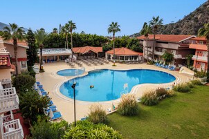 Ett semesterparadis med en stor pool, flera avslappningsområden och en imponerande bergskuliss.