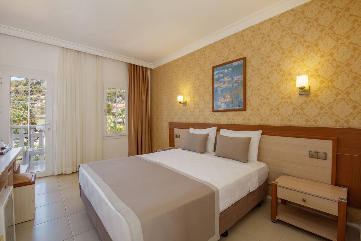 A hotel room with a large bed, a desk, and a view of the outdoors.
