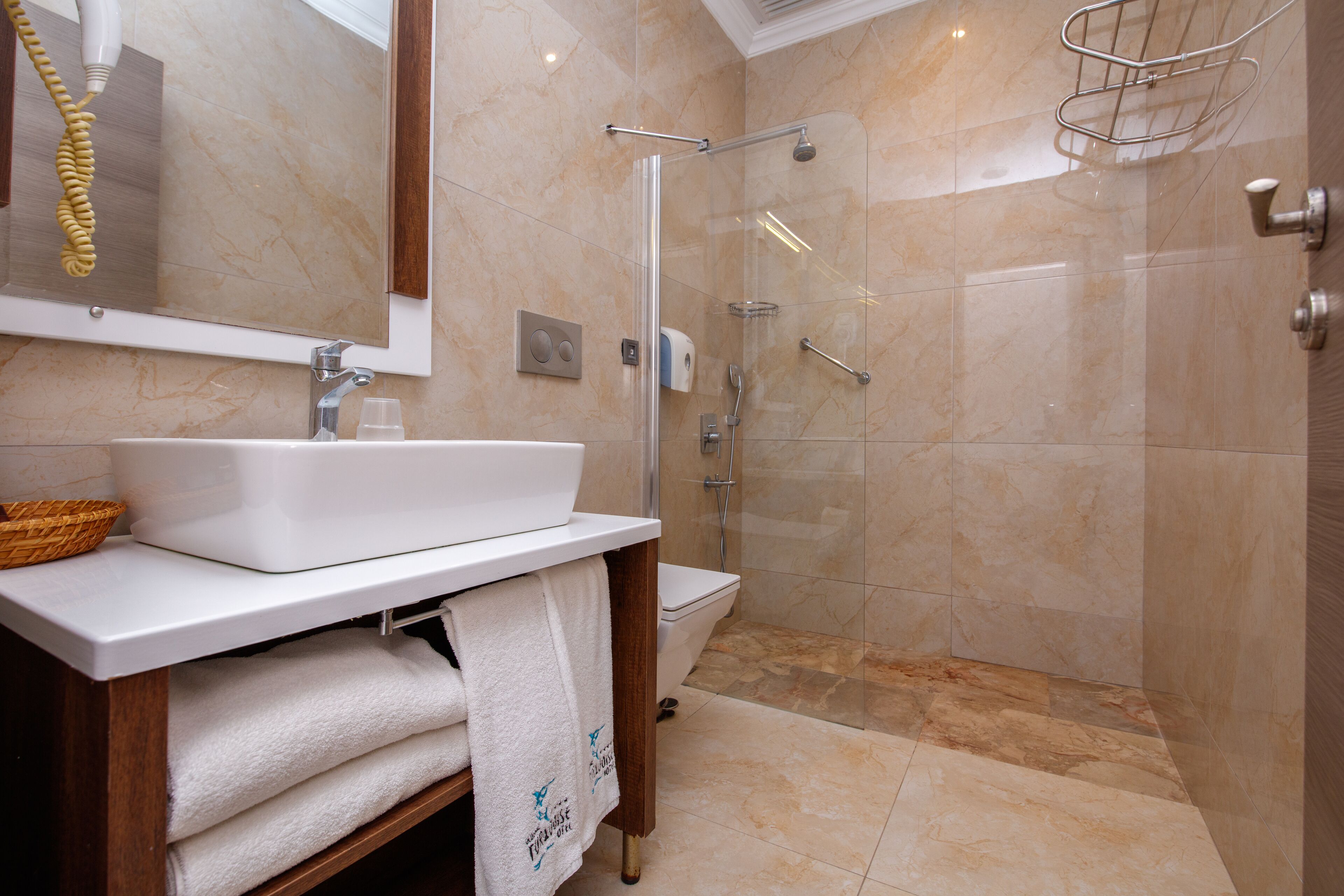 Un baño con lavamanos blanco, espejo y ducha con mampara de vidrio.