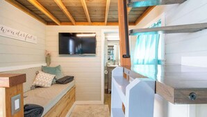 Une pièce chaleureuse avec un banc en bois, un téléviseur fixé au mur et un panneau sur lequel on peut lire : « La vie est belle ».