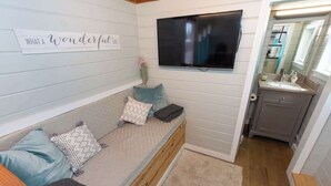 Une chambre de taille modeste, équipée d’un lit, d’un téléviseur fixé au mur et d’une petite salle de bain avec un lavabo et un miroir.