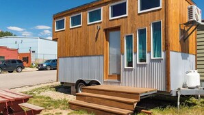 Une petite cabane en bois avec une porte d’entrée, plusieurs fenêtres et un petit porche.