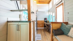 Une cuisine compacte avec des meubles en bois, un coin repas avec un banc et un petit espace détente avec des coussins.