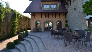 A stone building with a tiled patio, outdoor seating, and a stone wall with climbing plants. - Garni Hotel Chicha - Winery Skrbic (Belgrade)