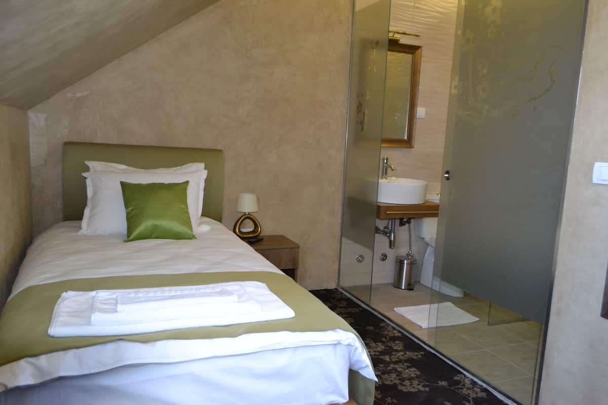 A hotel room with a bed, a nightstand, a bathroom with a sink and mirror, and a shower area.