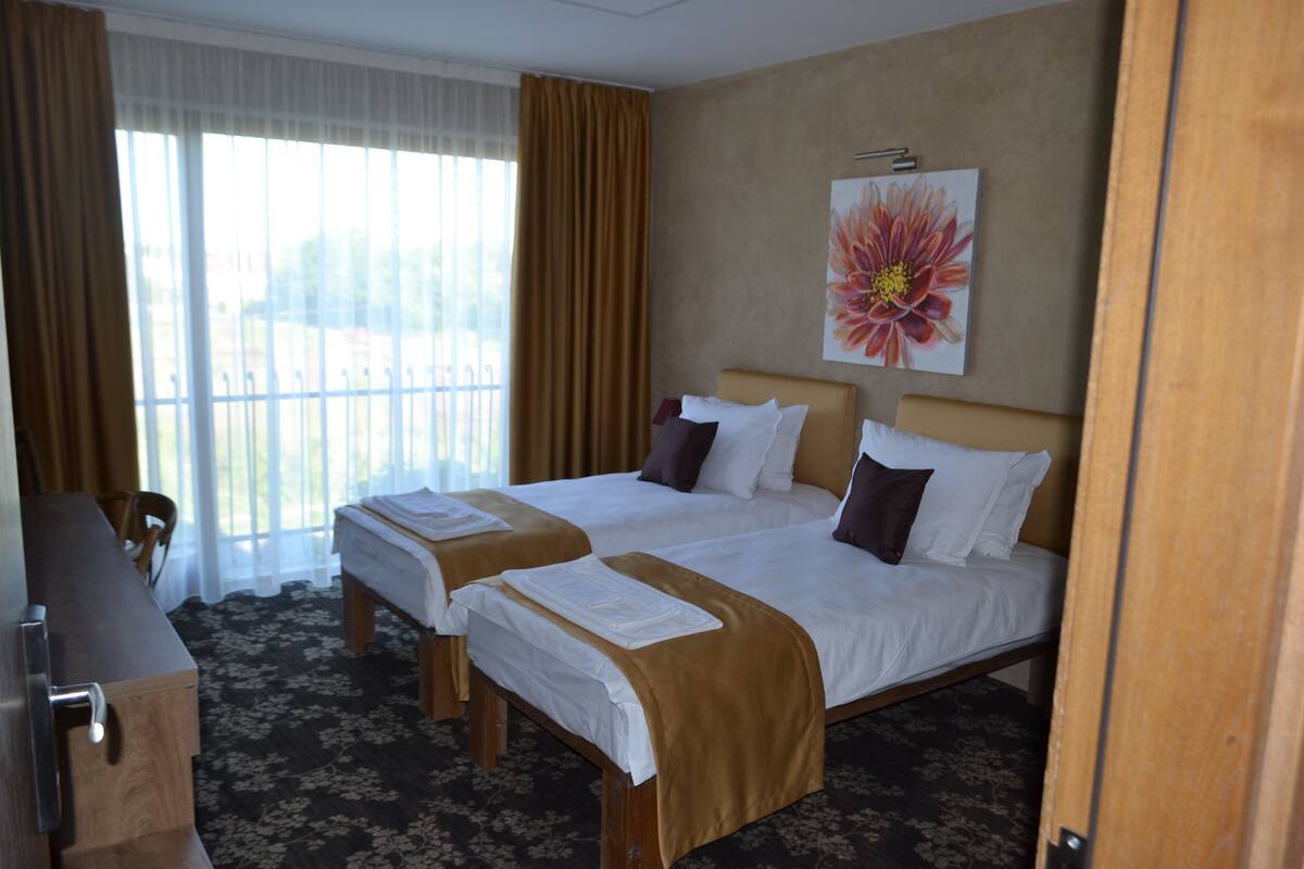 A hotel room with two beds, a desk, and a large window with curtains.