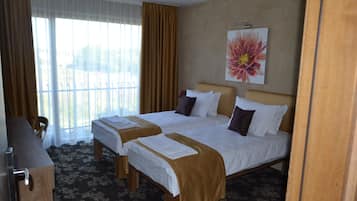 A hotel room with two beds, a desk, and a large window with curtains.
