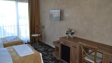 A hotel room with two beds, a wooden desk, a chair, and a painting on the wall.