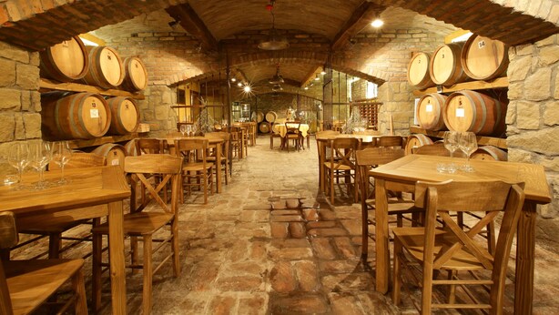 A cellar with wooden barrels, stone walls, and wooden tables and chairs. - Garni Hotel Chicha - Winery Skrbic (Belgrade)