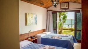 A hotel room with two beds, a wooden headboard, a nightstand, a lamp, and a view of the garden and sea through a glass door. - Village Paraiso Hotel (Florianópolis)