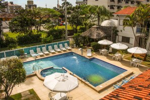 A swimming pool with lounge chairs and umbrellas, surrounded by greenery and buildings. - Village Paraiso Hotel (Florianópolis)
