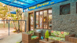 A building with a stone facade, a sign reading "Village Paraíso Resort," and outdoor wicker furniture with floral cushions. - Village Paraiso Hotel (Florianópolis)